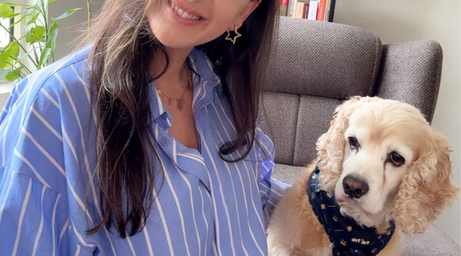Smiling woman sitting next to a cocker spaniel wearing a blue Pati Pets bandana with a crown pattern, creating a warm and stylish indoor moment.